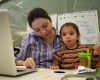 A mother works on her laptop while her child snacks on her lap.