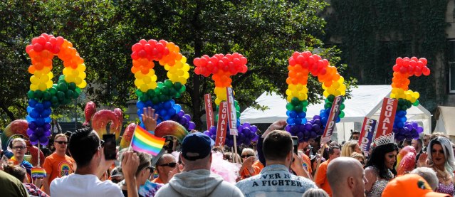 rainbow balloons spell out "PRIDE" over a crowd at an outdoor event